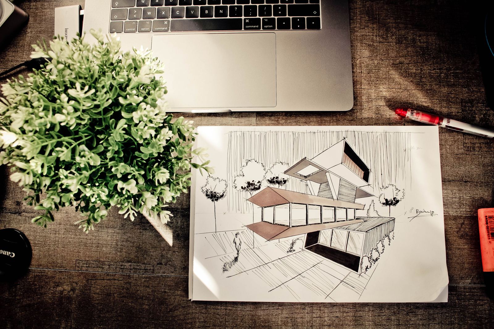 Croqui de arquitetura sobre a mesa, ao lado de um notebook e uma planta