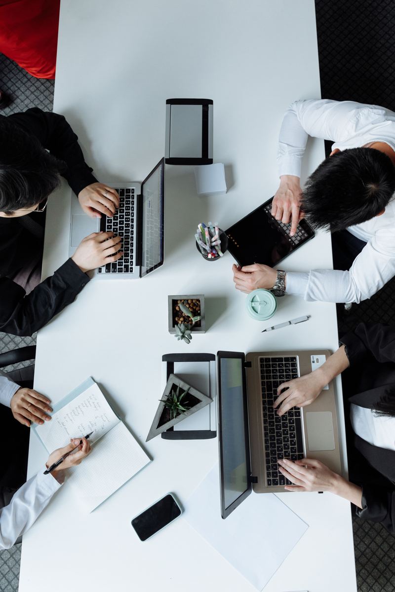 Vista de cima de uma equipe trabalhando com notebooks e cadernos numa mesa branca